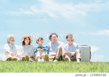 青空の見える公園・丘に座る家族・親子・三世代家族（父親・母親・娘・祖母・祖父） 129968186