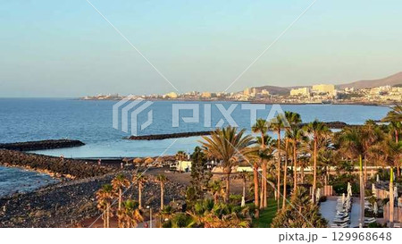 Experience the stunning view of the coastal landscape featuring palm trees at sunset 129968648