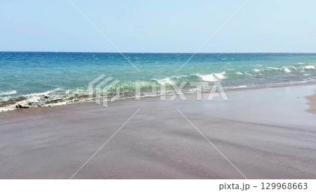 Serene Beach Waves Gently Lapping Against the Tranquil Shoreline Under Clear Blue Skies 129968663