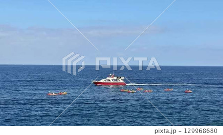 Adventurous individuals are kayaking near a motorboat amidst the beautiful, clear, and blue waters 129968680