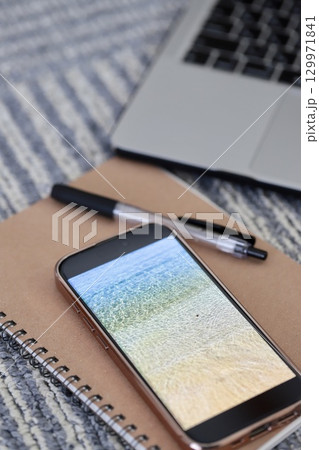 カーペットの上に置いたノートパソコンとスマホと筆記用具 129971841