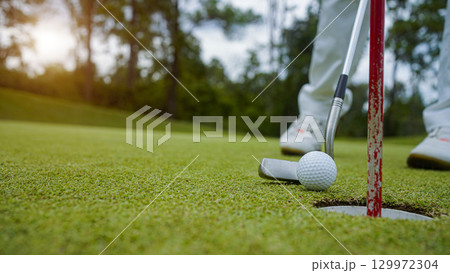Golfer putting ball on the green golf, lens flare on sun set evening time. Golfer hitting golf ball. 129972304