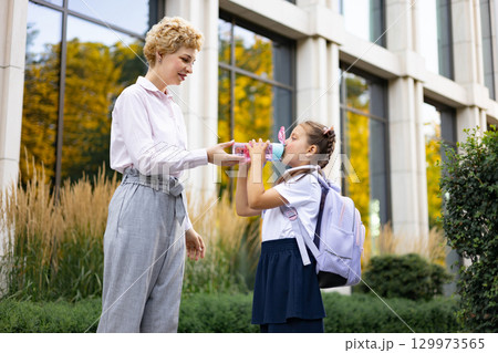 A mom offers water to her student daughter at the schoolyard. A mom offers water to her student daughter at the schoolyard. 129973565