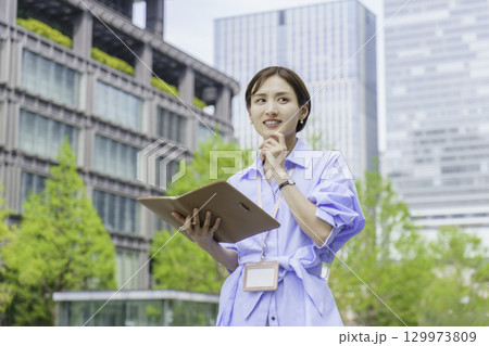 オフィス街で手帳を持って立つ若いビジネスウーマンのポートレート 129973809