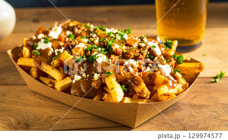 Canadian poutine served in a rustic bowl, crispy fries topped with cheese curds, rich brown gravy, and fresh herbs, paired with a cold glass of beer. Classic comfort food indulgence 129974577