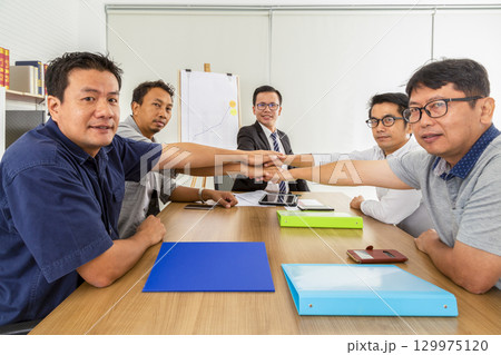Group of business people joining, holding hands showing teamwork in the office. Group of business people joining, holding hands showing teamwork in the office. 129975120