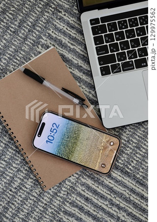カーペットの上に置いたノートパソコンとスマホと筆記用具 129975562