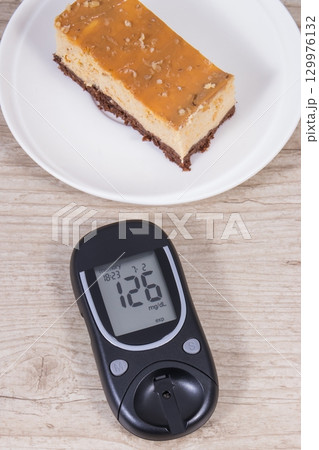 Glucometer and portion of cheesecake. Measuring and checking sugar level during diabetes Glucometer and portion of cheesecake. Measuring and checking sugar level during diabetes 129976132