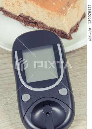 Glucometer for measuring and checking sugar level and piece of fresh baked sweet cheesecake Glucometer for measuring and checking sugar level and piece of fresh baked sweet cheesecake 129976133