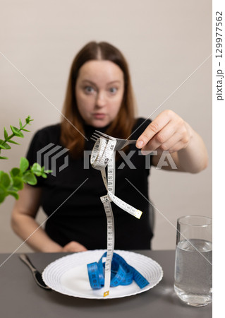 Person Shows Fork With Measuring Tape Instead of Food at Dining Table During Diet Reflection Person Shows Fork With Measuring Tape Instead of Food at Dining Table During Diet Reflection 129977562