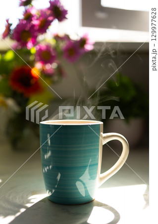 Steaming Cup of Coffee Beside Vibrant Flowers on a Sunny Morning Steaming Cup of Coffee Beside Vibrant Flowers on a Sunny Morning 129977628