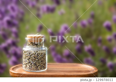 Glass Jar Filled with Dried Lavender on Wooden Tray with Lavender Background Outdoors 129978011