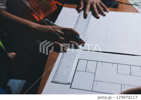 Closeup of team of industrial engineers meeting analyze machinery blueprints consult project on table in manufacturing factory. Working in manufacturing plant or production plant. Closeup of team of industrial engineers meeting analyze machinery blueprints consult project on table in manufacturing factory. Working in manufacturing plant or production plant. 129978217