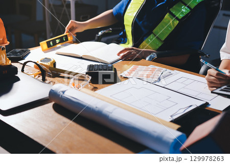 Closeup of team of industrial engineers meeting analyze machinery blueprints consult project on table in manufacturing factory. Working in manufacturing plant or production plant. Closeup of team of industrial engineers meeting analyze machinery blueprints consult project on table in manufacturing factory. Working in manufacturing plant or production plant. 129978263