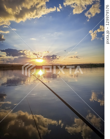 Early morning fishing. Fishing gear closeup on the river during sunset against the cloudy sky 129979576