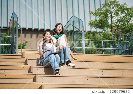友達と屋外の階段に座って佇む若い女性 129979686