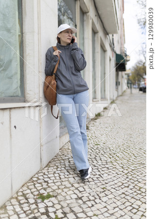 Delivery woman leaning against wall using smartphone in the city 129980039