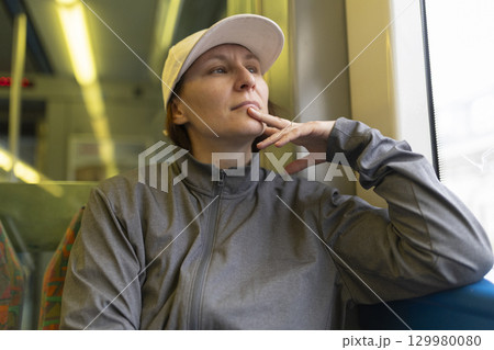 Pensive sportswoman wearing white cap contemplating during train journey 129980080