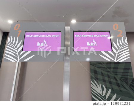 Self-service bag drop kiosks at airport with digital screens displaying instructions Self-service bag drop kiosks at airport with digital screens displaying instructions 129981221