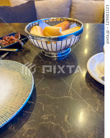 Breakfast in a cozy cafe. Fresh bread in a basket on a marble table. Breakfast in a cozy cafe. Fresh bread in a basket on a marble table. 129981323