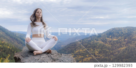 White woman meditates in lotus position on a stone cliff surrounded by autumn mountains in nature. A young woman practices yoga and fitness outdoor copy space White woman meditates in lotus position on a stone cliff surrounded by autumn mountains in nature. A young woman practices yoga and fitness outdoor copy space 129982393