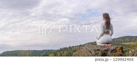 Woman in white clothes meditates on mountain during autumn, embracing nature and inner peace with a stunning view copy space panorama 129982408