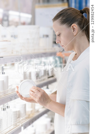 Woman in white attire selects porcelain dishes and bathroom accessories in a well-lit store. She holds a small porcelain plate in her hands. 129982454