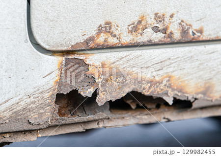 Rust on the door sills of an old car. Protection of cars from corrosion. Corroded car body showing significant rust damage and protective coatings wearing off in urban setting 129982455
