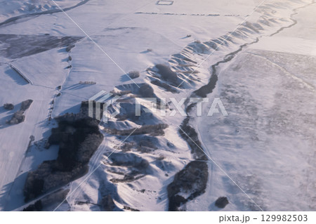 Aerial view shows a vast, pristine snowcovered landscape with hills and a winding river. Mountainous hilly snow-covered ridge imho aerial view. Minino, Krasnoyarsk Aerial view shows a vast, pristine snowcovered landscape with hills and a winding river. Mountainous hilly snow-covered ridge imho aerial view. Minino, Krasnoyarsk 129982503