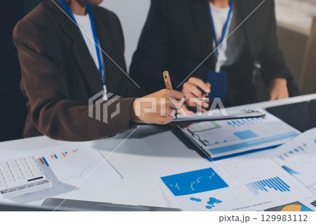 Focused young businessman signing agreement with skilled lawyer in eyeglasses. Concentrated financial advisor showing place for signature on paper contract document to male client at meeting in office 129983112