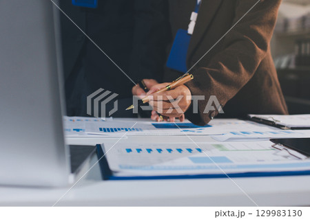 Focused young businessman signing agreement with skilled lawyer in eyeglasses. Concentrated financial advisor showing place for signature on paper contract document to male client at meeting in office 129983130