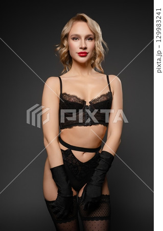Sensual woman in elegant lingerie poses confidently against a dark backdrop Sensual woman in elegant lingerie poses confidently against a dark backdrop 129983241