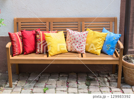 Wood romantic bench with a lot of multicolor pillows outdoor near stone house. 129983392
