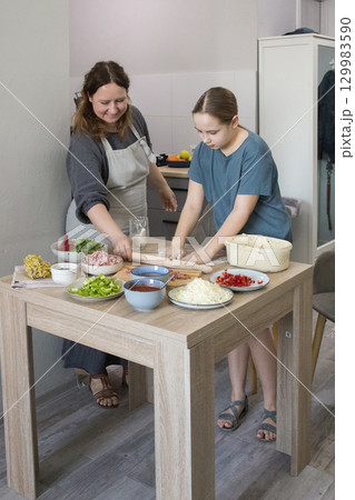 Young child girl daughter and mother preparing dough for pizza and smiling while baking 129983590