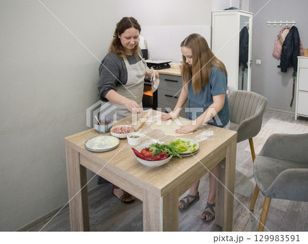 Pretty daughter cooking pizza with her mother in the kitchen 129983591