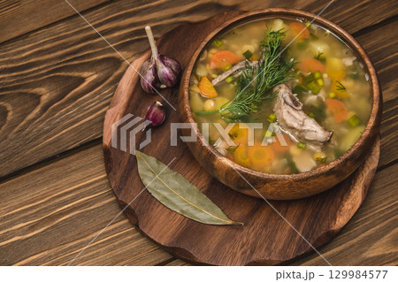 delicious homemade pea soup served in wooden bowl garlic and herbs on rustic wooden table. closeup. delicious homemade pea soup served in wooden bowl garlic and herbs on rustic wooden table. closeup. 129984577