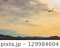 A single-engine aircraft tows a glider against the backdrop of mountains at sunset. 129984604
