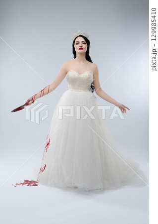 Bride in glamorous lingerie with knife, evoking beauty and horror at a wedding 129985410