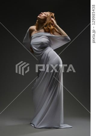 Sensual pose of a woman in lingerie with a flowing fabric draped around her 129985438
