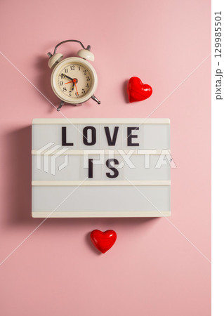 Word love is, with a red hearts and alarm clock, over pink background 129985501