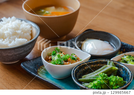 ご飯と味噌汁、納豆や温泉卵、野菜の小鉢を添えた和風朝食 129985667