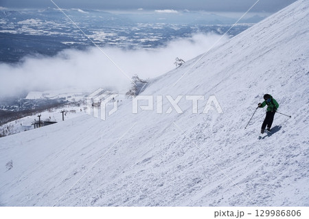ニセコ東急 グラン・ヒラフ・ゲレンデのダイナミックコースからスキー場管理区域を滑るスキーヤー 129986806