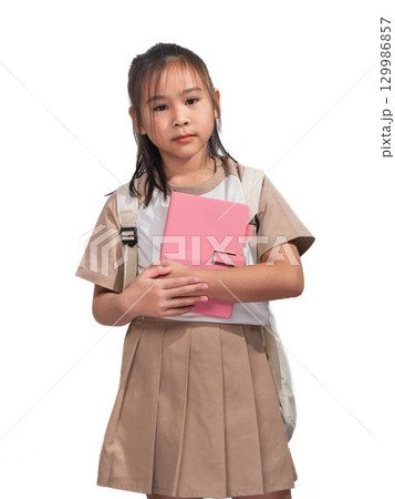 An Asian schoolgirl holding a pink notebook while carrying a backpack, wearing a student uniform and standing against a white background. An Asian schoolgirl holding a pink notebook while carrying a backpack, wearing a student uniform and standing against a white background. 129986857