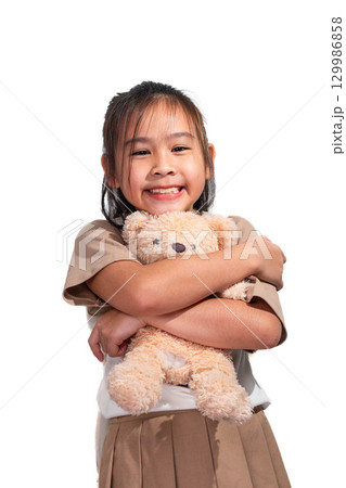 Asian girl smiling and hugging a teddy bear, showing a happy and playful expression against a white background. Asian girl smiling and hugging a teddy bear, showing a happy and playful expression against a white background. 129986858