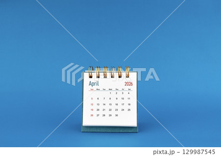 April 2026 mini desk calendar on blue color background. 129987545