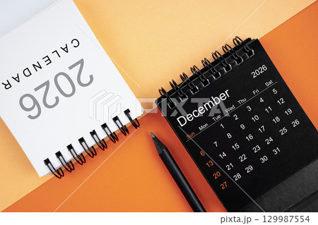 December 2026 desk calendar black and white color with pencil on orange color background. 129987554