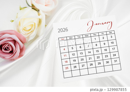 January 2026 calendar page and rose flower on white satin textile background. January 2026 calendar page and rose flower on white satin textile background. 129987855