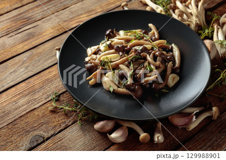 Fried shimeji mushrooms with thyme and garlic on a black plate. Fried shimeji mushrooms with thyme and garlic on a black plate. 129988901