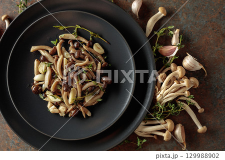 Fried shimeji mushrooms with thyme and garlic on a black plate. Fried shimeji mushrooms with thyme and garlic on a black plate. 129988902