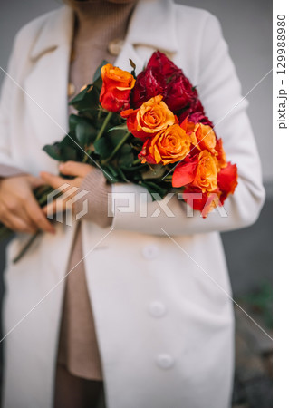 Woman holding a vibrant bouquet of roses in a stylish outfit outdoors 129988980